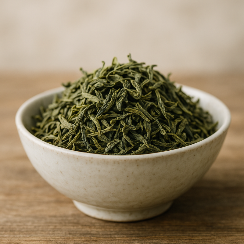 Organic loose green tea leaves in a white porcelain bowl on a wooden surface with soft natural lighting.